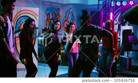 Young adults having fun partying, dancing and moving around on dance floor with stage lights. Cheerful friends doing funky dance moves having fun at underground party. Handheld shot. Young adults having fun partying, dancing and moving around on dance floor with stage lights. Cheerful friends doing funky dance moves having fun at underground party. Handheld shot. 105926758