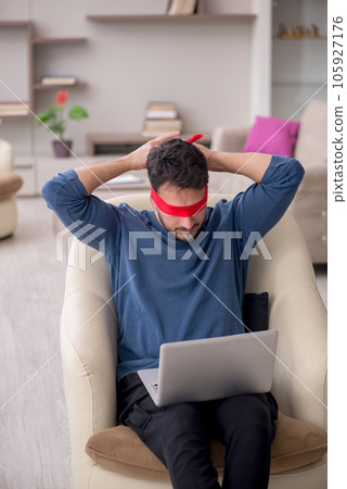 Blindfolded young male freelancer working from home 105927176