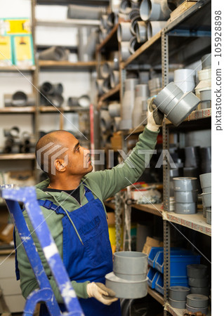 Salesman in overalls with plumbing fittings at hardware store warehouse Salesman in overalls with plumbing fittings at hardware store warehouse 105928898