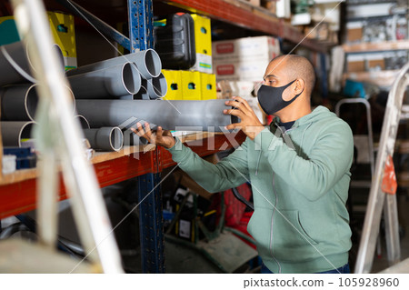 Craftsman in protective mask selects plastic plumbing pipes in hardware store 105928960