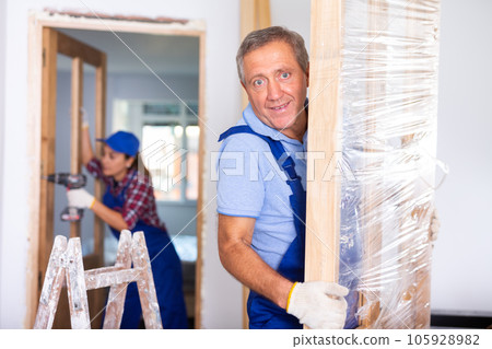 Man builder carrying new wooden door in apartment Man builder carrying new wooden door in apartment 105928982