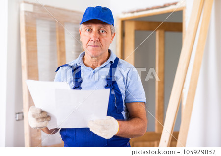 Serious middle-aged man in uniform exploring a plan of an apartment during renovation Serious middle-aged man in uniform exploring a plan of an apartment during renovation 105929032
