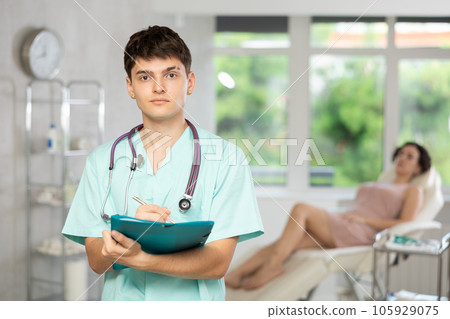 Young man doctor posing in doctor's cabinet with document in hands Young man doctor posing in doctor's cabinet with document in hands 105929075