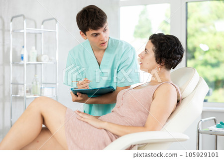 Young male doctor signing papers while talking with woman patient Young male doctor signing papers while talking with woman patient 105929101