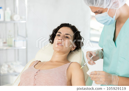 Middle-aged woman having arm injection lying on clinical chair Middle-aged woman having arm injection lying on clinical chair 105929119