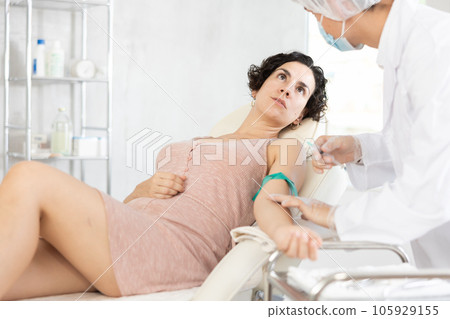 Middle-aged woman having vein injection lying on clinical chair Middle-aged woman having vein injection lying on clinical chair 105929155