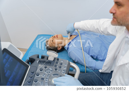 Middle aged woman patient during ultrasound examination of thyroid lying on couch in medical office Middle aged woman patient during ultrasound examination of thyroid lying on couch in medical office 105930852
