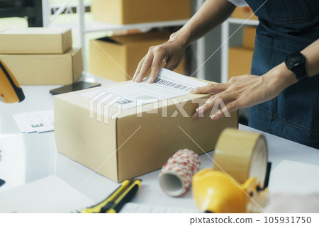 Young business owner putting shipping label on parcel.. Young business owner putting shipping label on parcel.. 105931750