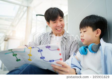 Happy cheerful Asian family traveling in the downtown together concept. Father looking at the railway station map with his son and pointing a forefinger on the map. Asian family tourist in city. 105931829