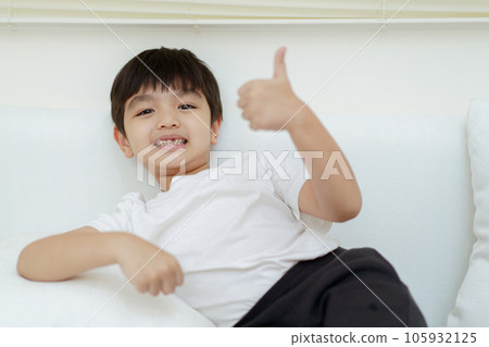 Happy cheerful Asian little young boy sits on the sofa and plays with camera, a little boy looking and smiling to camera. Happy cheerful Asian little young boy sits on the sofa and plays with camera, a little boy looking and smiling to camera. 105932125