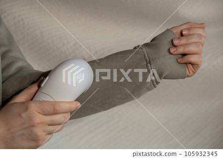 Woman using Anti-pilling razor at home. Device for shaving pellets clothes. Anti-Plush fabric Shaver. Electric portable sweater pill defuzzer Lint remover from acrylic or wool sweater. Sustainability 105932345