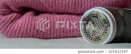 Anti-pilling razor. Device for shaving clothes. Anti-Plush fabric Shaver. Electric portable sweater pill defuzzer Lint remover from pink acrylic or wool sweater. Electric device fabric shaver after 105932347