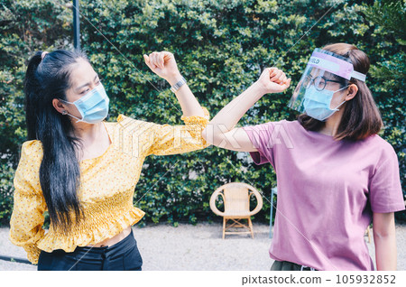 Two woman bump elbows for greeting during coronavirus epidemic. The elbow bump was suggested as an alternative way for reduce your risk of spreading or contracting the virus. 105932852
