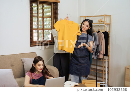 Beautiful asian woman showing clothes for sale in front of camera for live streaming at home Beautiful asian woman showing clothes for sale in front of camera for live streaming at home 105932868