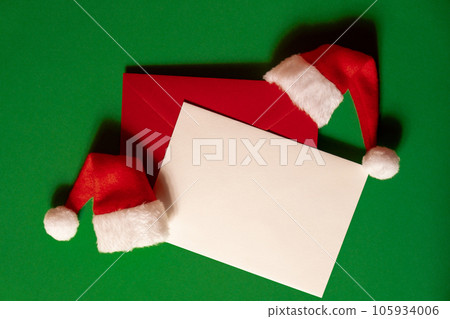 Santa hat with empty paper card note envelope on green background. Copy space for your text. Mock up for advertisement. Holiday Christmas composition 105934006
