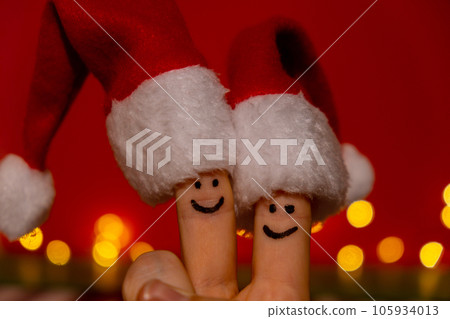 Fingers dressed in Santa-Claus red-white hats. Two happy finger smileys faces representing social network on red background. Copy space for your text Happy family celebrating concept for Christmas or 105934013
