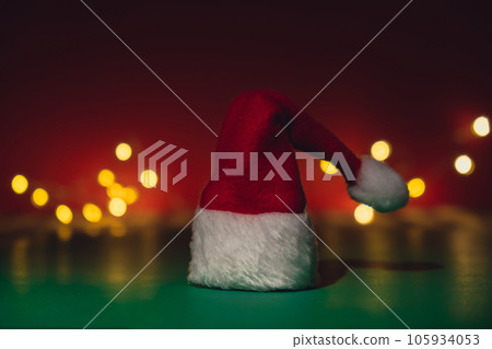 Santa hat on isometric green red background. Defocused lights on backdrop Copy space for your text. Mock up for advertisement. Holiday Christmas composition. Minimalistic greeting card Santa hat on isometric green red background. Defocused lights on backdrop Copy space for your text. Mock up for advertisement. Holiday Christmas composition. Minimalistic greeting card 105934053