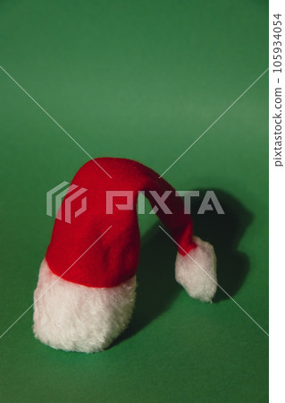 Santa hat on isometric green red background. Copy space for your text. Mock up for advertisement. Holiday Christmas composition. Minimalistic greeting card Santa hat on isometric green red background. Copy space for your text. Mock up for advertisement. Holiday Christmas composition. Minimalistic greeting card 105934054