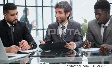 three colleagues of modern work co-working space talking and smiling while sitting at the desk table with laptop computer 105934506