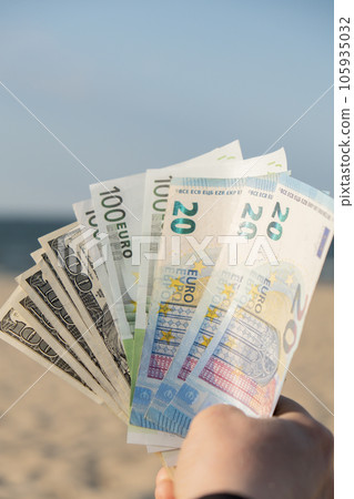 Unrecognizable woman Displaying Spread of Cash euros and dollars bills on sandy beach coastline. Concept finance saving money for holiday vacation. Costs in travel holidays. Extra money 105935032