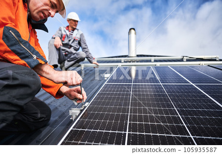 Workers installing photovoltaic solar panels on roof of house. Men engineers in helmets building solar module system with help of hex key. Concept of alternative, renewable energy. Workers installing photovoltaic solar panels on roof of house. Men engineers in helmets building solar module system with help of hex key. Concept of alternative, renewable energy. 105935587