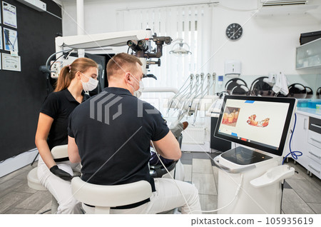 Dentist scanning patient's teeth with modern machine for intraoral scanning. Digital print of patient's teeth is on big screen. Modern high precision technologies. Concept of modern dentistry Dentist scanning patient's teeth with modern machine for intraoral scanning. Digital print of patient's teeth is on big screen. Modern high precision technologies. Concept of modern dentistry 105935619