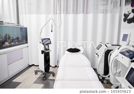 Interior of beautician cabinet with modern cosmetology equipment for skincare rejuvenation treatment and salon chair. Radiofrequency microneedling device, patient daybed and laser machine in clinic. 105935623