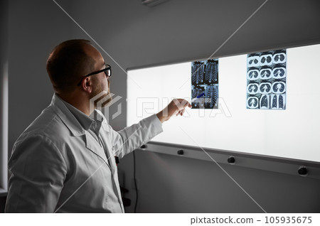Side view of doctor studying MRI results. Male specialist working in clinic, carrying out description of the radiographs of a patient, pointing by pen. Concept of medicine and healthcare. Side view of doctor studying MRI results. Male specialist working in clinic, carrying out description of the radiographs of a patient, pointing by pen. Concept of medicine and healthcare. 105935675