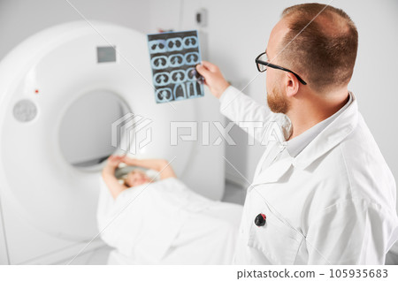 Medical computed tomography or MRI scanner. Close up of doctor holding and examining results of MRI. Woman patient lying on couch. Concept of medicine, healthcare and modern diagnostics. 105935683