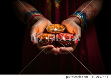 Woman hands with henna holding colorful clay diya lamps lit during diwali celebration 105937351