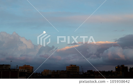 Lush cumulus clouds float across the evening sky with the moon on a warm summer evening over urban high-rise buildings. Concept natural phenomenon. Copyspace Lush cumulus clouds float across the evening sky with the moon on a warm summer evening over urban high-rise buildings. Concept natural phenomenon. Copyspace 105938642
