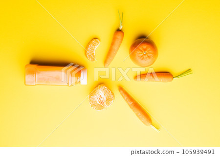 Close up of bottle with juice, carrots and tangerines with copy space on yellow background 105939491