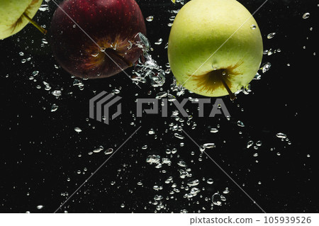 Close up of apples falling into water with copy space on black background 105939526