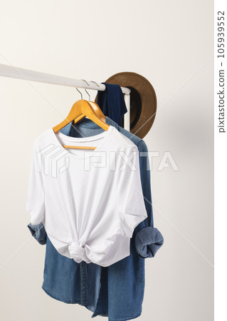 White t shirt, hat and denim shirt hanging from clothes rail with copy space on white background White t shirt, hat and denim shirt hanging from clothes rail with copy space on white background 105939552