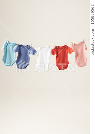 Multi coloured baby grows hanging from clothes line with pegs and copy space on white background 105939568