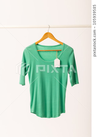 Green t shirt with tag on hanger hanging from clothes rail with copy space on white background 105939585