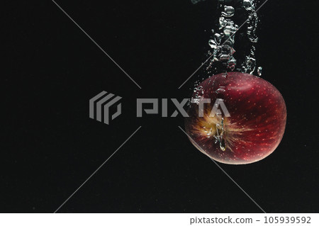 Close up of red apple falling into water with copy space on black background 105939592