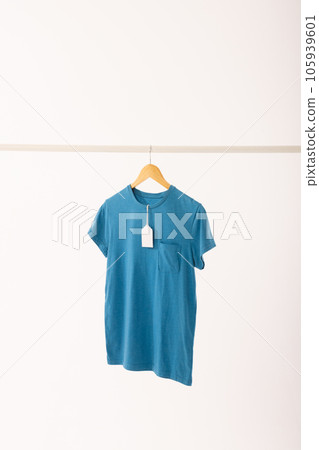 Blue t shirt with tag on hanger hanging from clothes rail with copy space on white background Blue t shirt with tag on hanger hanging from clothes rail with copy space on white background 105939601