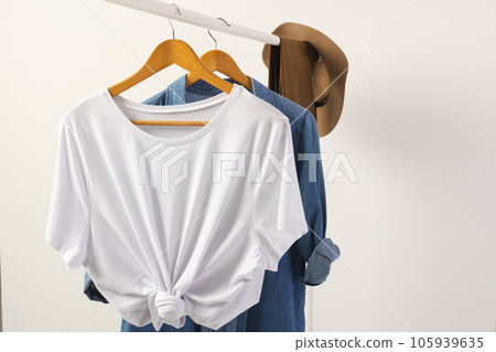 White t shirt, hat and denim shirt hanging from clothes rail with copy space on white background White t shirt, hat and denim shirt hanging from clothes rail with copy space on white background 105939635