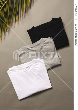Three t shirts and palm tree leaf with copy space on grey floor background 105939673