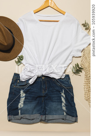 Flat lay of white t shirt, sunhat, net bag and denim shorts with copy space on cream background 105939920