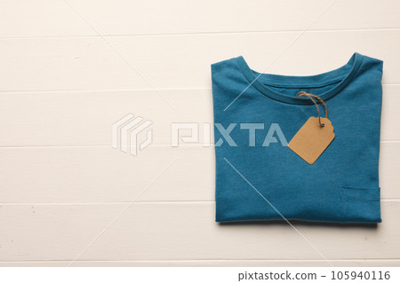 Close up of flat lay of blue t shirt with tag and copy space on white boards background Close up of flat lay of blue t shirt with tag and copy space on white boards background 105940116