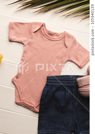 Flat lay of pink baby grow, shorts, dummy and pink booties with copy space on white background 105940139