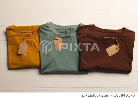 Close up of flat lay of three t shirts with tags and copy space on white boards background Close up of flat lay of three t shirts with tags and copy space on white boards background 105940170