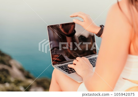 Freelance women sea working on the computer. Good looking middle aged woman typing on a laptop keyboard outdoors with a beautiful sea view. The concept of remote work. 105942075