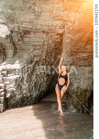 Woman swimsuit sea. Attractive blonde woman in a black swimsuit enjoying the sea air on the seashore around the rocks. Travel and vacation concept. 105942159