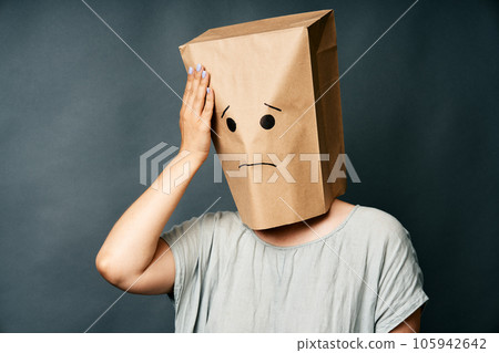 Woman with hand on head and upset smile on the paper bag on head 105942642