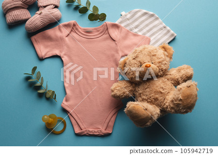 Flat lay of pink baby grow, hat, teddy bear and pink booties with copy space on blue background Flat lay of pink baby grow, hat, teddy bear and pink booties with copy space on blue background 105942719