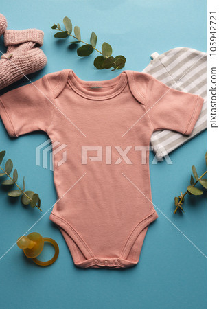 Flat lay of pink baby grow, hat, dummy and pink booties with copy space on blue background Flat lay of pink baby grow, hat, dummy and pink booties with copy space on blue background 105942721