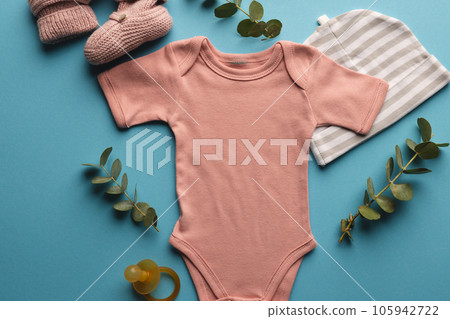 Flat lay of pink baby grow, hat, dummy and pink booties with copy space on blue background Flat lay of pink baby grow, hat, dummy and pink booties with copy space on blue background 105942722